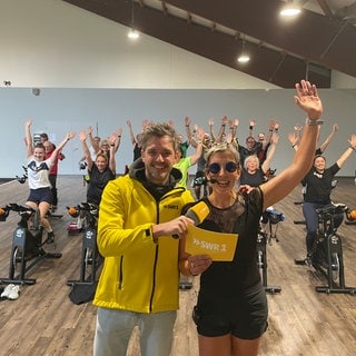 Silke und Benedikt vor dem Spinningkurs, der die Arme nach oben werfen vor Freude