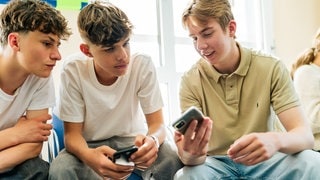 Drei Schüler schauen auf ein Smartphone