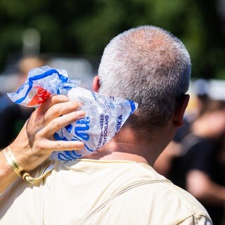 Ein Mann steht in der Sonne, mit einem kühlendem Eisbeutel am Nacken.