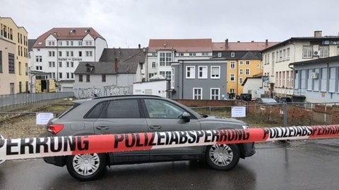 Ein Auto steht hinter einem Absperrband der Polizei im Hintergrund befindet sich der Tatort, ein Hinterhof in der Offenburger Innenstadt.