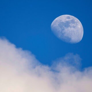 Der Mond am blauen Taghimmel über einer weißen Wolke: Warum ist der Mond auch tagsüber zu sehen?