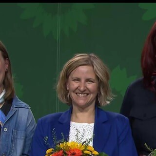 Drei Frauen der Partei Die Grünen mit Blumensträußen auf der Bühne