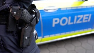 Ein Polizist steht vor einem Einsatzfahrzeug (Symbolbild): Ein Fall von Swatting hat in Neustadt einen Großeinsatz ausgelöst