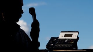 Ein Mann posiert mit einem Telefon (Symbolbild). Telefonbetrüger haben eine Seniorin um ihr Erspartes gebracht. Sie legte Schmuck vor die Haustür. 