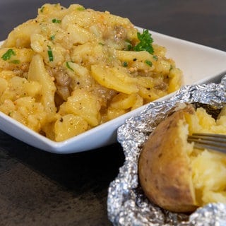 Karroffelsalat aus gegrillten Kartoffeln in ener Schale angerichtet und daneben ein Folien-Kartoffel frisch vom Grill.