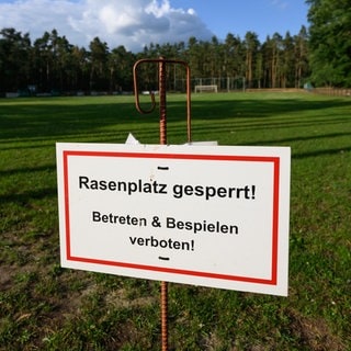 Ein Schild „Rasenplatz gesperrt!“ steht an einem Fußballplatz.