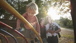 Beispielbild für Eltern mit Kindern auf dem Spielplatz in der Sonne