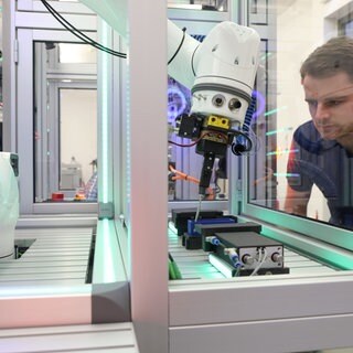 Mehr Start-ups für die Westpfalz, dieses Ziel verfolgt das Netzwerk "Southwest X". In der Smart Factory Kaiserslautern wird Innovationsfreude schon heute gelebt: Der Forschungsverein entwickelt gemeinsam mit Unternehmen Systeme für automatisierte Produktionsprozesse. Eine Produktionsanlage mit Greifarm im Vordergrund, im Hintergrund beobachtet ein Mitarbeiter des Forschungsvereins Smart Factory Kaiserslautern die Abläufe.
