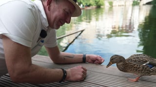 Eine Ente und ein kniender Mann auf einem Floss 