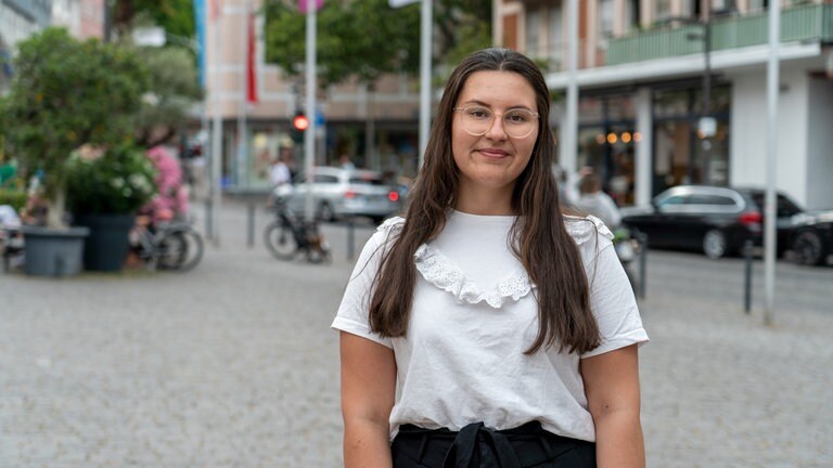 Eine junge Frau mit Brille steht auf dem Wormser Marktplatz und lächelt in die Kamera.