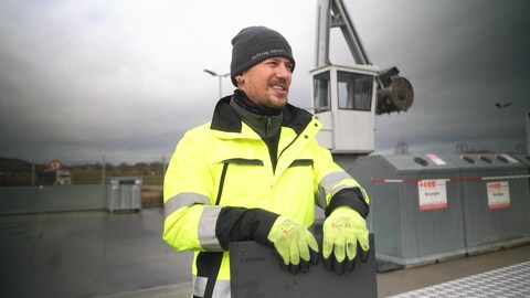Arno Heinzmann steht auf einem Wertstoffhof. Er trägt eine neongelbe Warnweste. 