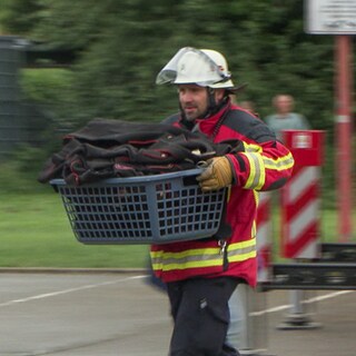 Ein Feuerwehrmann in Ausrüstung trägt einen Korb mit Feuerwehrausrüstung. 