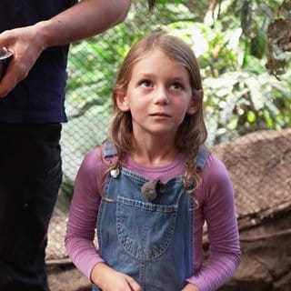 Die achtjährige Lena möchte Zoodirektorin werden. Sie steht in einem Gehege im Karlsruher Zoo und trägt eine Latzhose und ein rosa Langarmshirt.