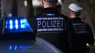 Symbolbild: Polizeieinsatz mit Festnahme: Polizisten, die vor einem Blaulicht stehen