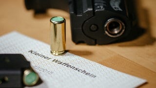 Ein Kleiner Waffenschein liegt zwischen einer Schreckschuss-Pistole "Walther P22", einem Magazin und einer Knallpatrone. Das Dokument berechtigt den Besitzer zum Tragen einer solchen Waffe in der Öffentlichkeit. 
