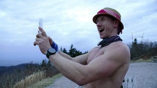 Ultraläufer Daniel Hernes filmt sich selbst mit einem Handy. Sein Oberkörper ist nackt und er trägt einen Hut.
