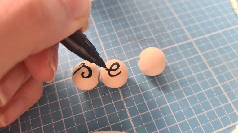 Je nach Begriff können die Holzperlen beschriftet werden. Dabei eine Perle pro Buchstabe wählen und diese mit schwarzem Lackstift beschriften.