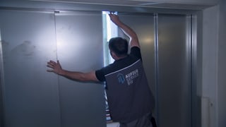 Techniker öffnet von Hand eine Aufzugstür zu einem Autoaufzug