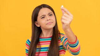Mädchen hält skeptisch ein Dragee in die Höhe: Kinder brauchen für ihre gesunde Entwicklung Vitamine und Mineralstoffe. Aber was, wenn sie sie nicht über die Nahrung aufnehmen können oder wollen? Dann gibt es Nahrungsergänzungsmittel. Aber bei welchen Kindern ist die Nahrungsergänzung wirklich sinnvoll und welche Eltern sollten lieber die Finger davon lassen?