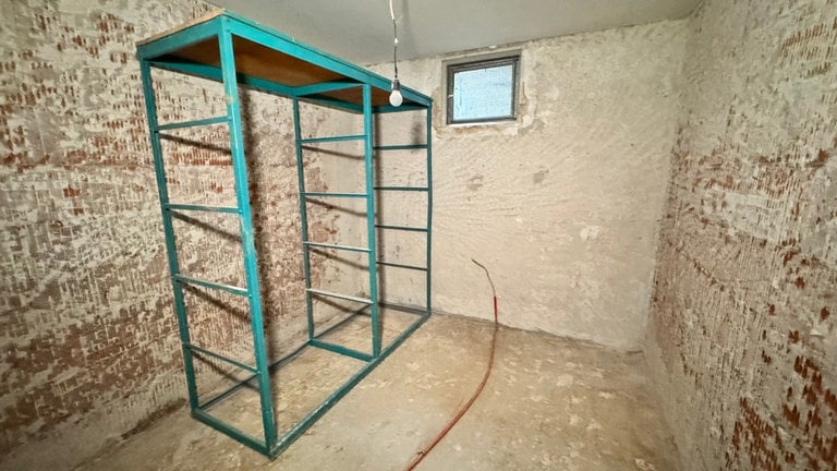Ein türkises Regal steht in einem leeren Raum. Die Wände wurden bis auf die Backstein mauer entkernt.