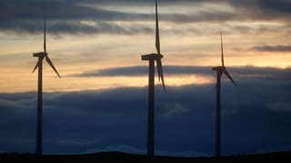 Drei Windräder vor Himmel und dunklen Wolken.