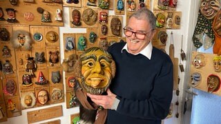 Gerold Weschenmoser aus Starzach-Bierlingen hält lächelnd eine Maske im Arm. Hinter ihm hängen zahlreiche kleine Masken an der Wand. Er hält den Weltrekord im Miniaturmaskensammeln.