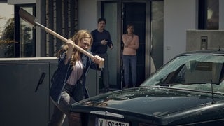 v. li. Anja Schneider als Jenni, im Hintergrund  Dominik Weber und Christiane Bärwald als Sven und Mara Giebert. Jenni schlägt mit einem Spaten das Auto des Paares Giebert kaputt. 