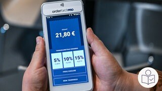 Das Bild zeigt ein Bezahlterminal für Kartenzahlung. Das Display zeigt die Gesamtsumme. Darunter sind jeweils große Auswahlfelder für 5%, 10% und 15%. Wiederum darunter und kleiner die Auswahlfelder für freie Eingabe und kein Trinkgeld. Rechts unten das SWR-Logo für Leichte Sprache.