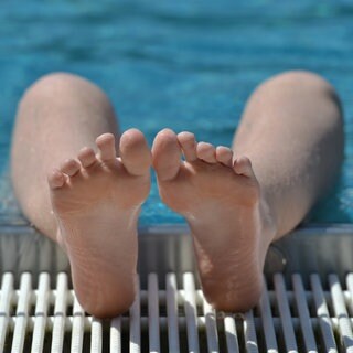 Füße und Unterschenkel am Beckenrand von jemandem, der im Schwimmbecken abgetaucht ist