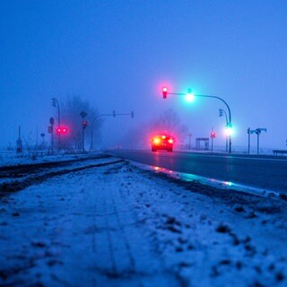 Ein Auto steht am Morgen auf einer teilweise vereisten Bundesstraße an einer Ampelkreuzung. Das Wetter am Wochenende wird zwar etwas wärmer, teilweise Schnee und Regen führen aber zu Glätte.