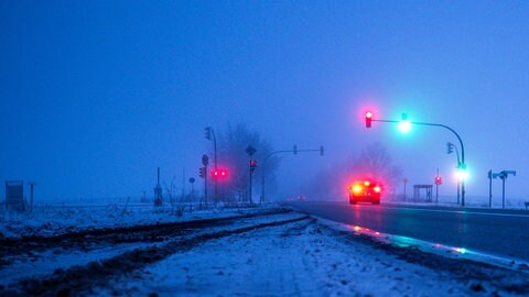 Ein Auto steht am Morgen auf einer teilweise vereisten Bundesstraße an einer Ampelkreuzung. Das Wetter am Wochenende wird zwar etwas wärmer, teilweise Schnee und Regen führen aber zu Glätte.