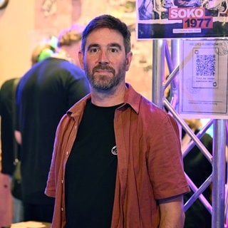 Der Geschäftsführer des Computerspielstudios Paintbucket Games, Jörg Friedrich, steht bei der Gamescom am Messestand der Bundeszentrale für politische Bildung, an dem sein Spiel Soko 1977 gezeigt wird.   Seine Vorliebe für Computerspiele fand Jörg Friedrich in seiner Jugend – über den legendären Heimcomputer C64. Jetzt ist der gebürtige Heilbronner selbst Spiele-Entwickler. Seine Spezialität: "Serious Games" – Spiele, die gesellschaftlichte Themen vermitteln. In SWR1 Leute erzählt er über sein neuestes Projekt: "Eine Nacht im Moka Efti", ein Game zur TV-Serie "Babylon Berlin"