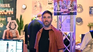 Der Geschäftsführer des Computerspielstudios Paintbucket Games, Jörg Friedrich, steht bei der Gamescom am Messestand der Bundeszentrale für politische Bildung, an dem sein Spiel Soko 1977 gezeigt wird.   Seine Vorliebe für Computerspiele fand Jörg Friedrich in seiner Jugend – über den legendären Heimcomputer C64. Jetzt ist der gebürtige Heilbronner selbst Spiele-Entwickler. Seine Spezialität: "Serious Games" – Spiele, die gesellschaftlichte Themen vermitteln. In SWR1 Leute erzählt er über sein neuestes Projekt: "Eine Nacht im Moka Efti", ein Game zur TV-Serie "Babylon Berlin"