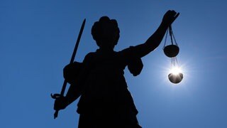 Die Silhouette der Justitia-Statue auf dem Römerberg in Frankfurt am Main zeichnet sich gegen Sonne ab. Dabei hat es den Anschein, als läge die Sonne in Ihrer Gerechtigkeitswaage.