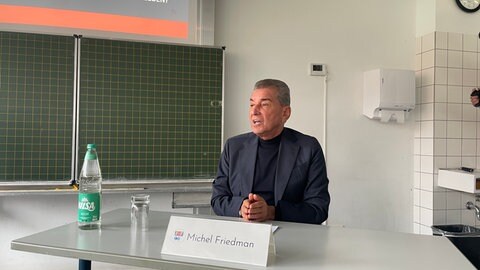 Michel Friedman sitzt an einem Pult. Der Publizist hat das Otto-Schott-Gymnasium im Rahmen des ARD-Jugendmedientags besucht. 