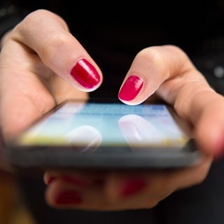 Eine Person tippt mit beiden Händen auf ihr Handy, Fingernägel sind rot lackiert. Ein Mann aus dem Rems-Murr-Kreis ist auf sogenanntes "Love Scamming" auf einer Dating Plattform reingefallen. Laut dem Polizeipräsidium Aalen hat er einer Person, die sich online als Notärztin ausgegeben hat, rund 2,3 Millionen Euro überwiesen. Kurz nach dem er das Geld überwiesen habe, brach die betrügerische Person den Kontakt ab. 