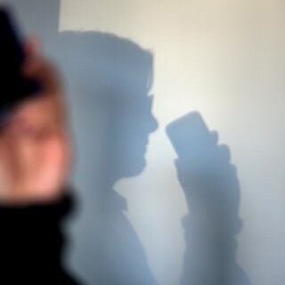 Jemand telefoniert mit dem Mobiltelefon, an der Wand zeichnet sich ein Schatten ab.