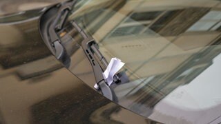 Strafzettel klemmt hinter Scheibenwischer an dunklem Auto. Das Geschäft mit Strafzetteln.