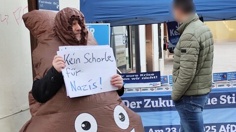 Mann protestiert in Neustadt in einem Kostüm, das wie ein Kackhaufen aussieht