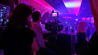 Clubszene im Dunkeln. Menschen tanzen zu blaulila Lichtern. Kamera filmt tanzende Menschen.