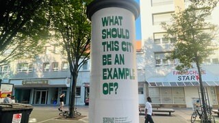 "What should this city be an example of?" steht groß auf einer Litfaßsäule in Ludwigshafen. Das Ganze ist eine Aktion des Ludwigshafener Kunstvereins.
