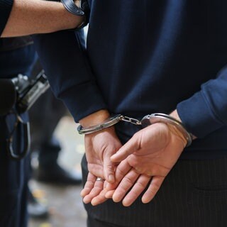 Ein Polizist führt einen Verdächtigen Mann mit Handschellen ab. (Symbolbild)