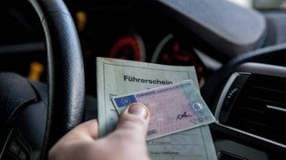 Person hält im Auto seinen Führerschein in der Hand