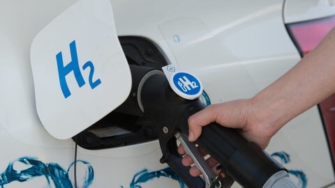 Der Tankdeckel Autos mit der Aufschrift "H2" für Wasserstoff steht offen und der Tank wird an einer Zapfsäule befüllt. (Symbolbild)