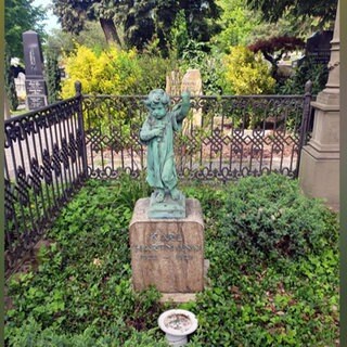 Eine türkise Bronzestatue eines Engels steht auf einem Grabstein auf einem Friedhof.