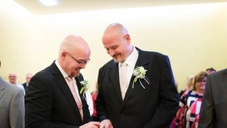Ralf Gockel und Bernd Barkholt-Gockel stecken sich bei ihrer Eheschließung im Rathaus von Hamm in Nordrhein-Westfalen gegenseitig die Eheringe an - beide tragen feierliche Hochzeitsanzüge mit Ansteck-Blumen.