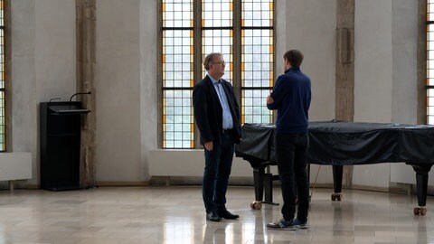 Dekan Torsten Krannich steht mitten in einem großen, kirchlichen Gebäude und ist im Gespräch mit einem SWR-Reporter. Er befasst sich mit dem Psychoterror in Langenau und steht im Kontakt mit Pfarrer Ralf Sedlak.
