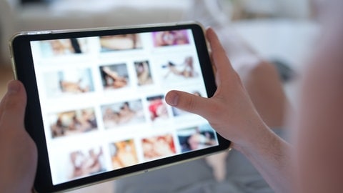 Ein junger Mann schaut sich auf einem Smartphone eine Porno-Internetseite an (gestellte Szene)