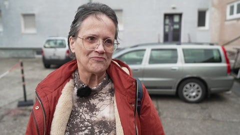 Dame mit einer roten Winterjacke und kurzen braunen Haaren und roter Jacke steht auf einem Hinterhof-Parkplatz.