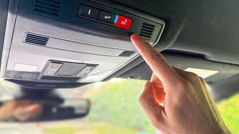 Mann drückt mit dem Finger auf einen SOS-Knopf im Auto